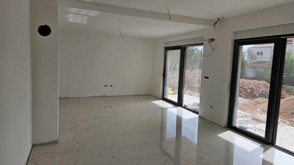 Interiér s veľkou plochou okien, bielymi stenami a dláždenou podlahou, stále vo výstavbe.