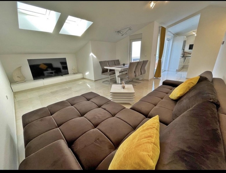 Moderná obývacia izba so strešnými oknami, veľkou pohovkou, jedálenským stolom a televíziou.