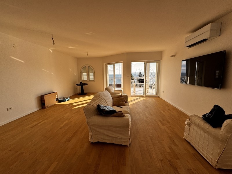 Svetlá obývacia izba s bielou pohovkou, nástennou TV a panoramatickými oknami s výhľadom na more