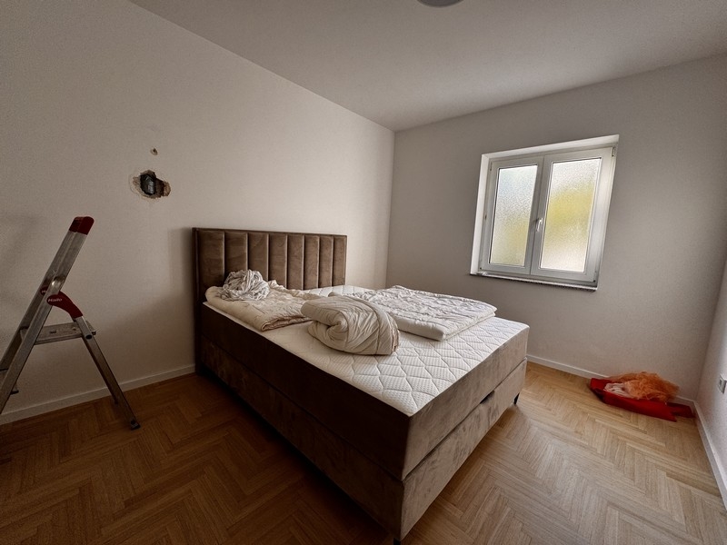 Spálňa s veľkou čalúnenou posteľou, bielymi prikrývkami a malým oknom