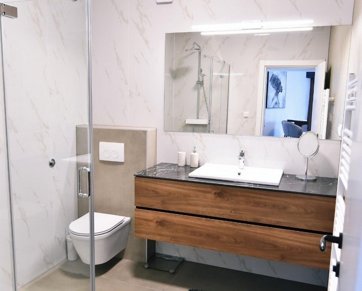 Moderná kúpeľňa so sprchovacím kútom, umývadlom a drevenou komodou.