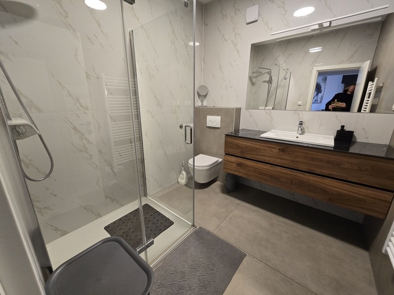 Priestranná kúpeľňa so sprchovacím kútom, umývadlom a elegantnými obkladmi.