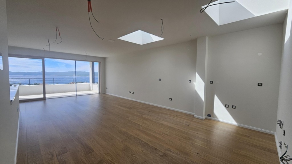 Obývacia izba zaliata svetlom s výhľadom na more a parketovými podlahami