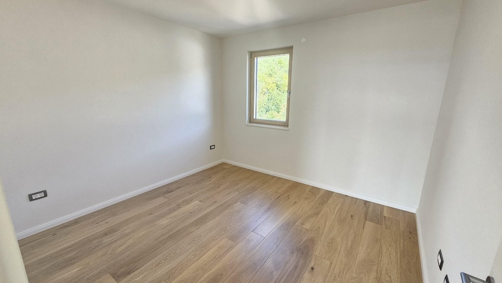 Svetlá spálňa s drevenými podlahami a výhľadom z okna do zelene