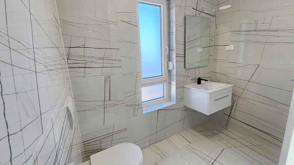 Moderná vydláždená kúpeľňa s oknom, umývadlom a WC