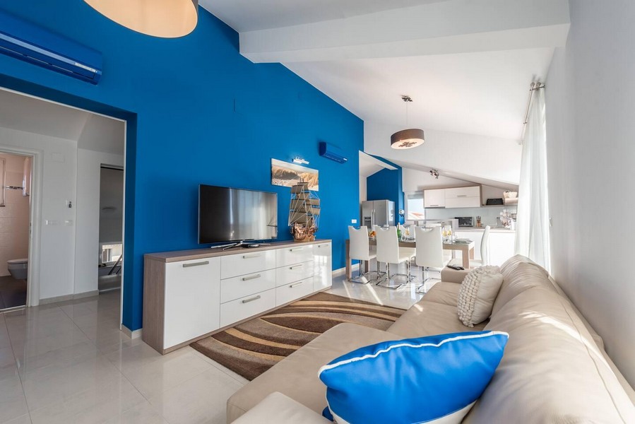 Obývacia izba s modrou stenou a otvorenou kuchyňou