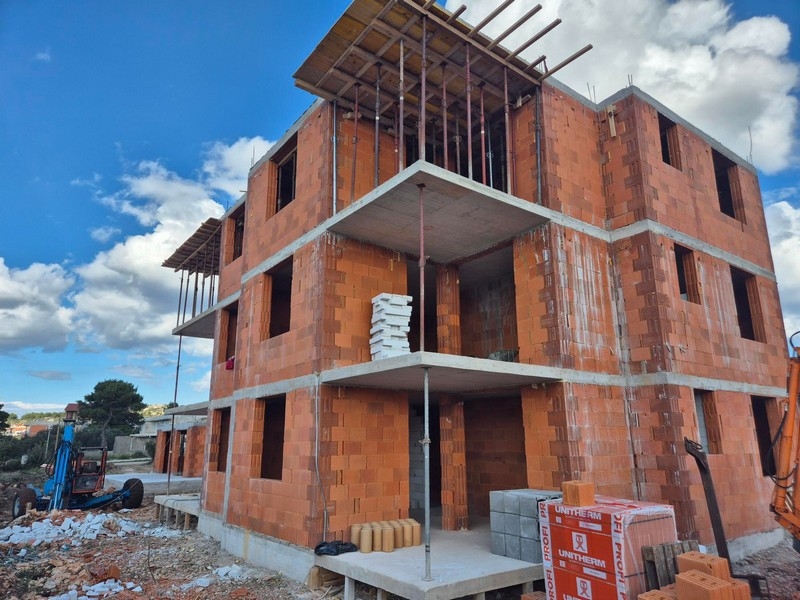 Novostavba trojpodlažného obytného domu s otvorenými balkónmi a stavebnými materiálmi