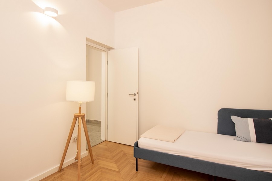 Druhá spálňa so stojacou lampou a drevenou podlahou