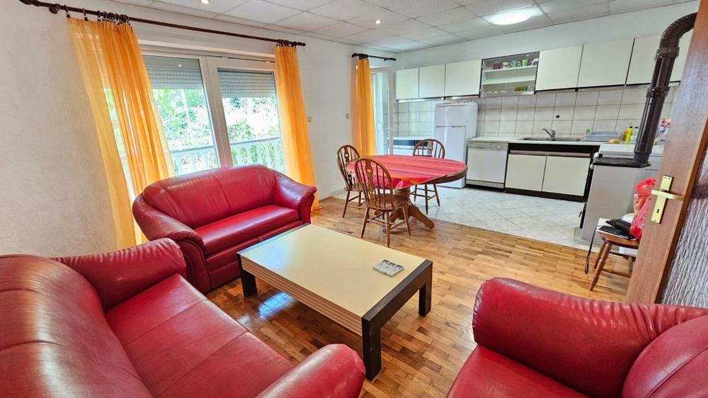 Obývacia izba s červenou koženou pohovkou, prístupom na balkón a otvorenou kuchyňou