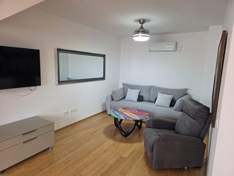 Obývacia izba so sivým gaučom, kreslom a nástenným zrkadlom