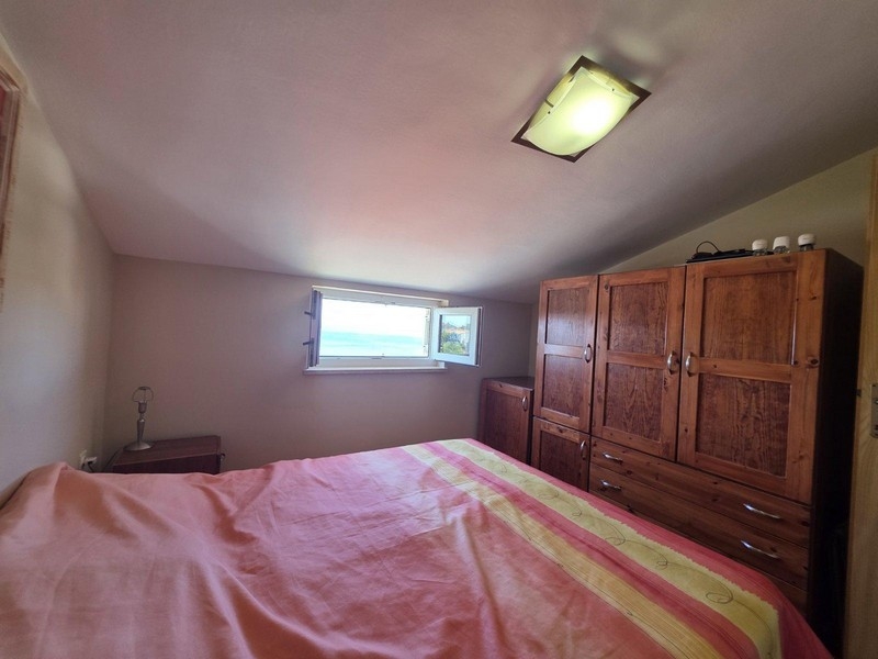 Spálňa s manželskou posteľou a oknom s výhľadom na more.