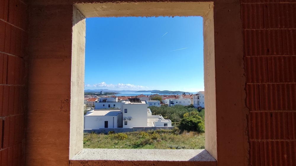 Pohľad cez nedokončené okná na more a obytnú štvrť