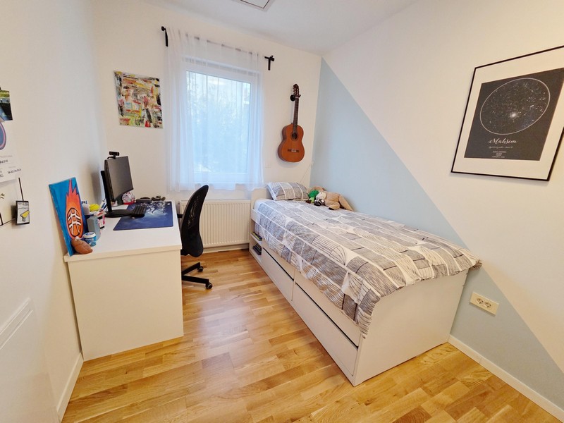 Izba pre mladých s písacím stolom, posteľou a gitarou na stene