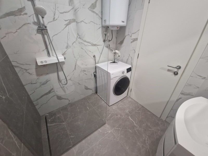 Kúpeľňa so sprchovacím kútom na úrovni podlahy a práčkou