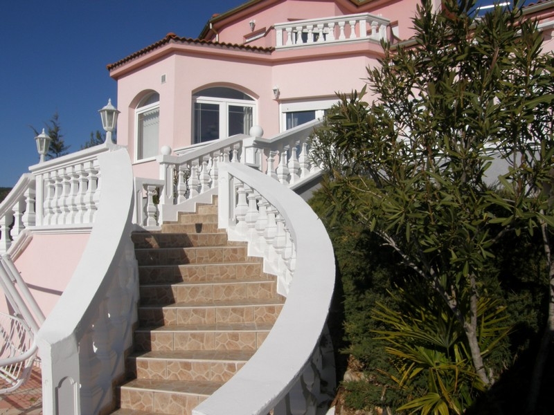 Pohľad spredu na ružovú vilu v Chorvátsku s kľukatými bielymi schodmi a stredomorskou vegetáciou