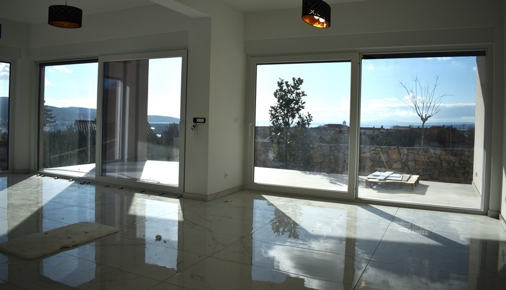 Priestranná, prázdna obývacia izba s bielymi stenami a veľkým oknom vo vile na Krku.