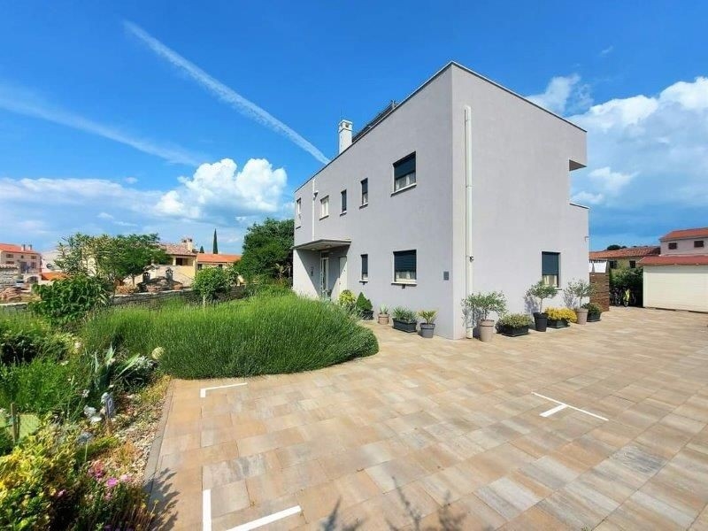 Pohľad spredu na moderný trojbytový dom na predaj na Istrii s vydláždeným predzáhradkou a obklopený rastlinami v kvetináčoch.