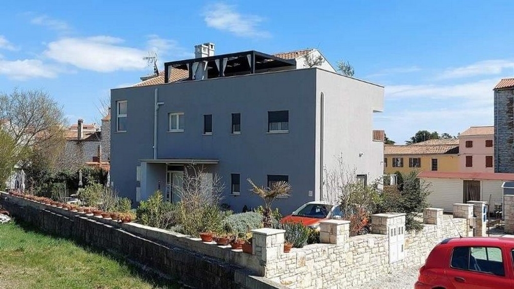 Bočný pohľad na trojbytový dom na predaj na Istrii s terasou a rastlinnou výzdobou pozdĺž plotu.