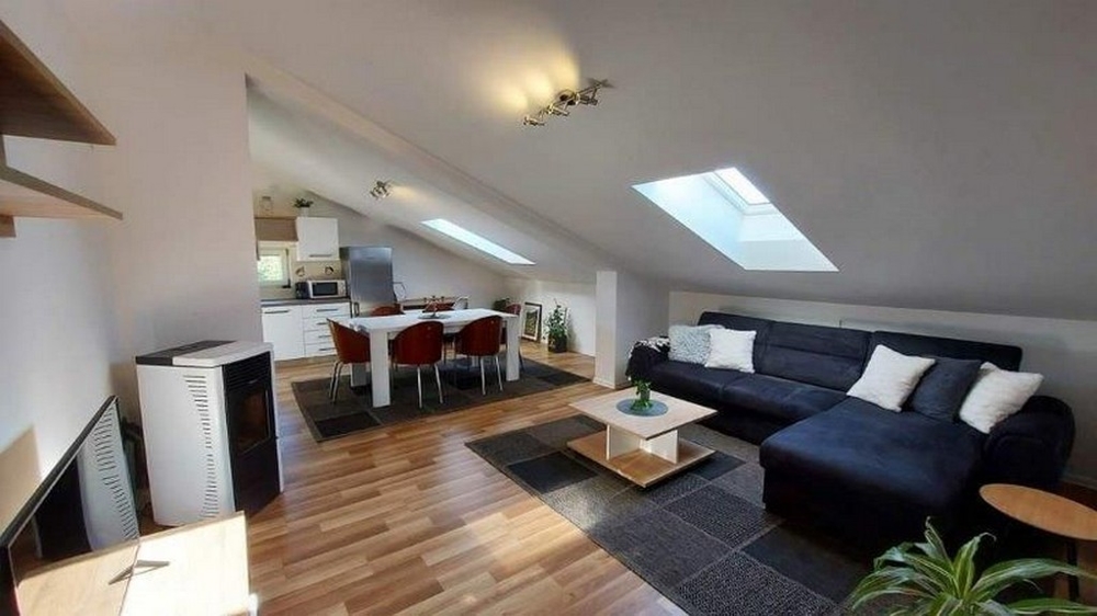 Útulná obývačka v podkroví domu s tromi apartmánmi na Istrii, na predaj, s pohovkou, jedálenským stolom a otvorenou kuchynkou.