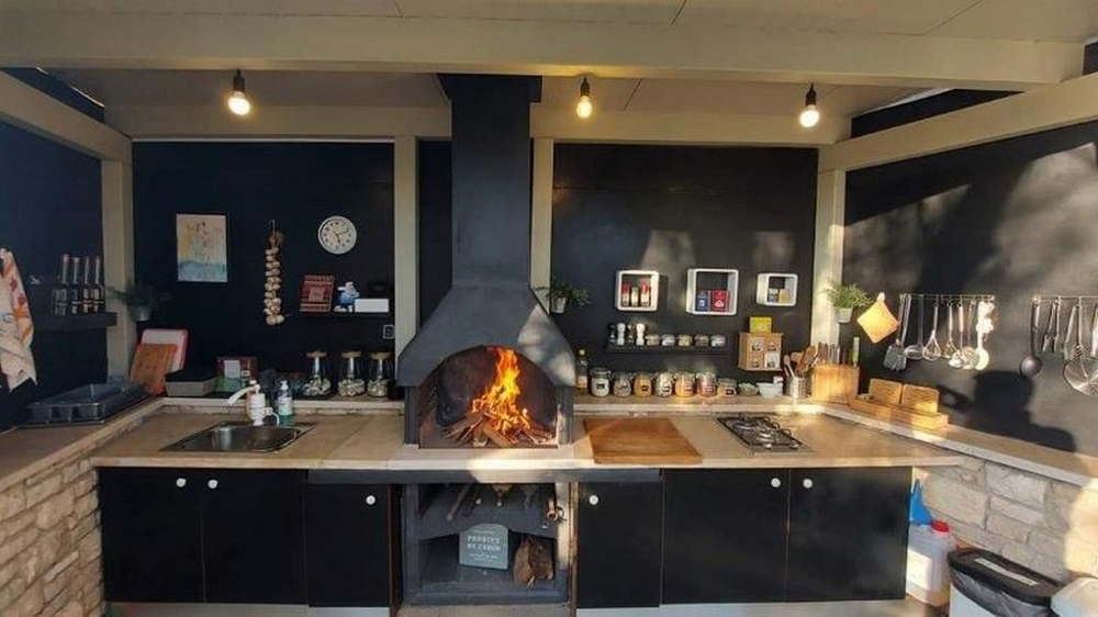 Kuchyňa s krbom na grilovanie v dome s tromi apartmánmi na Istrii, na predaj, s čiernymi pracovnými plochami a modernými kuchynskými spotrebičmi.