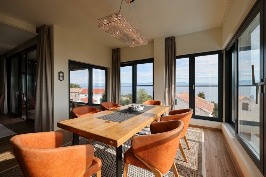 Jedálenský kút s dreveným stolom, oranžovými stoličkami a výhľadom na more vo vile na predaj na Ugljan.
