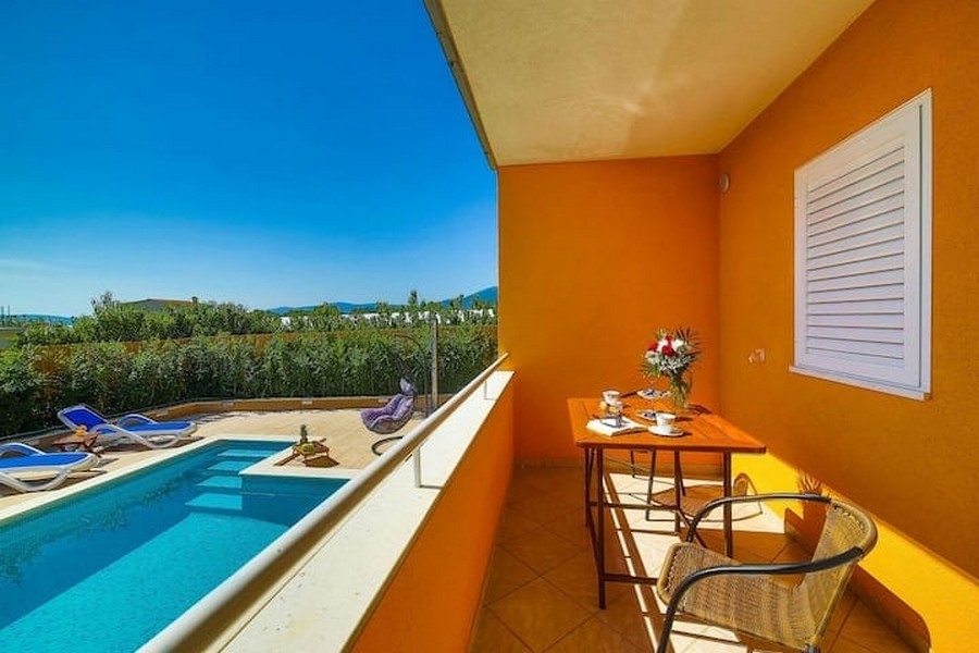 Výhľad z balkóna na bazén v bytovom dome v Kaštel Lukšić, Chorvátsko, so stolom a stoličkami