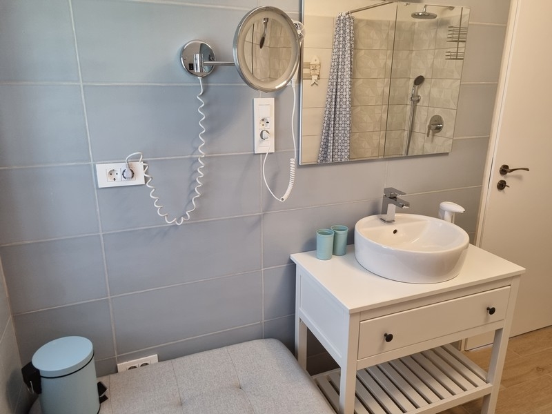 Kúpeľňa v prímorskom bytovom dome na predaj v Karlobagu, Chorvátsko, so svetlomodrými dlaždicami, bielou konzolou na umývanie, zrkadlom a vešiakom na uteráky