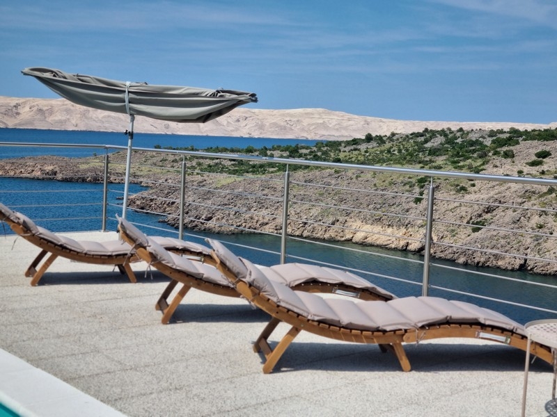 Relaxačná zóna s ležadlami a slnečníkom na terase apartmánového domu v chorvátskom Karlobagu s výhľadom na more.