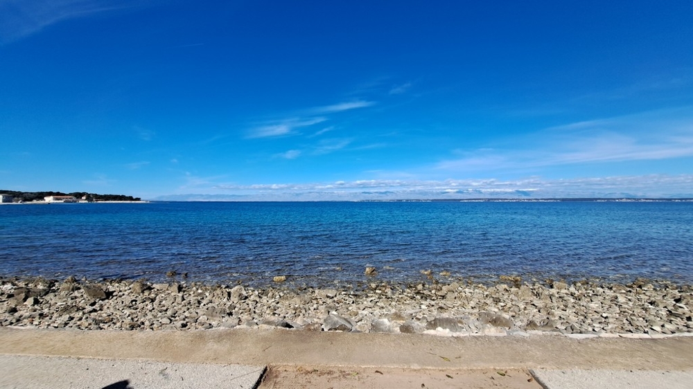 Kamienková pláž a čisté more pred prímorskou nehnuteľnosťou v Chorvátsku