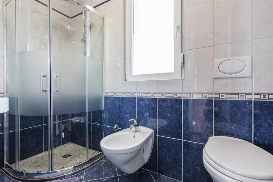 Kúpeľňa v nehnuteľnosti v Chorvátsku, bytový dom s výhľadom na more, s rohovou sprchou, bidetom a WC, svetlé steny a tmavomodré obklady