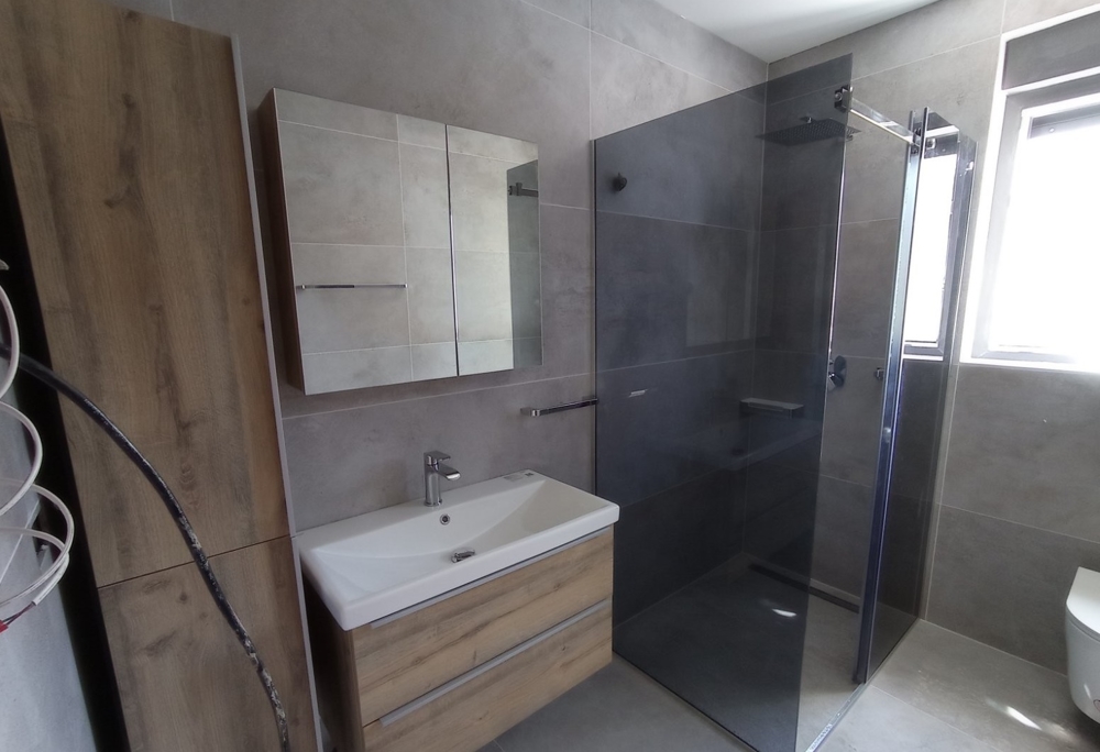 Moderná kúpeľňa so sprchovacím kútom v nehnuteľnosti v Chorvátsku, zrkadlová skrinka a drevené prvky v dizajne.