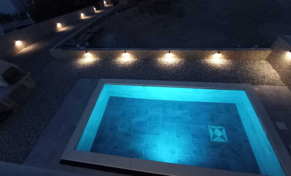 Nočný pohľad na bazén s modrým osvetlením a čiastočný výhľad na nehnuteľnosť v Chorvátsku v pozadí.