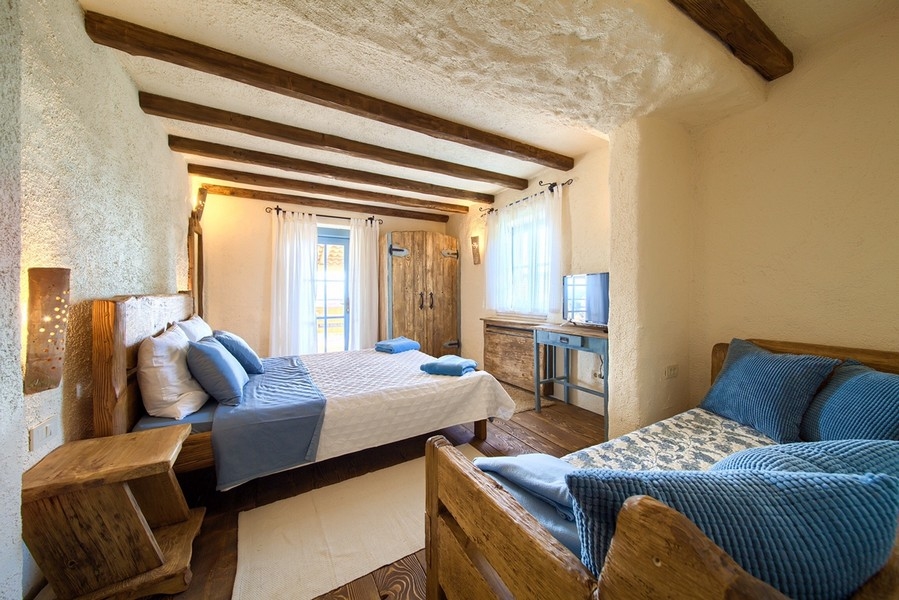 Útulná spálňa s rustikálnym dreveným nábytkom a prirodzeným osvetlením, príjemným aspektom majetku ostrova Krk.