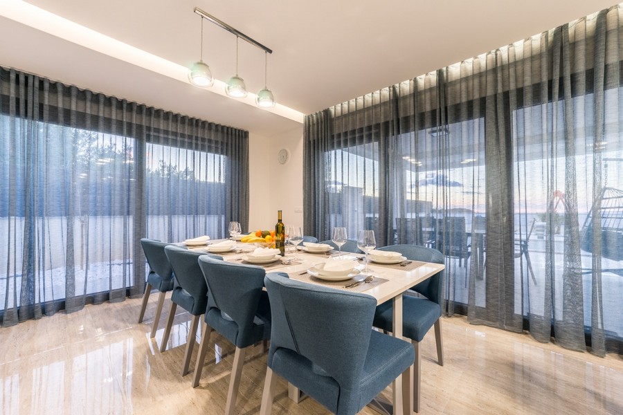 Elegantný jedálenský kút s veľkými oknami, ktoré ponúkajú prirodzené svetlo a výhľad na vašu vysnívanú nehnuteľnosť v Chorvátsku.