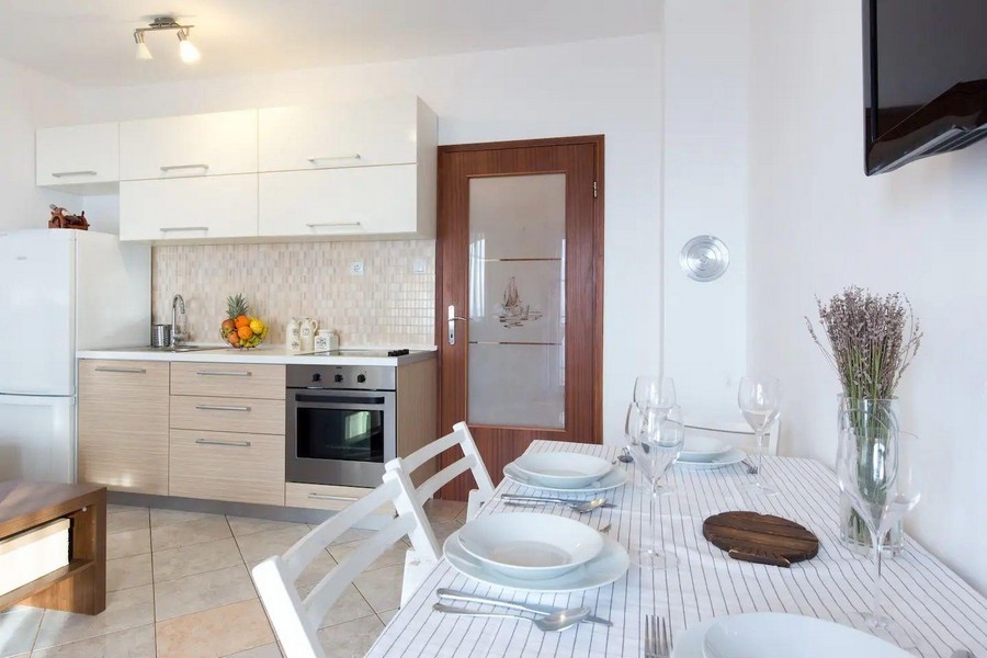 Moderná kuchyňa a jedálenský kút s bielymi a drevenými skrinkami, prestretým jedálenským stolom a výhľadom do obývacej časti.