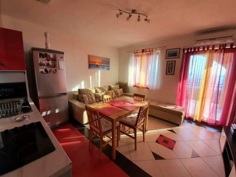 Slnečný obývací a jedálenský kút s červenými a žltými akcentmi, vybavený jedálenským stolom, pohovkou a prístupom na balkón.