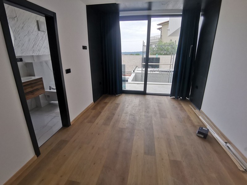 Pohľad do interiéru spálne s drevenými podlahami a veľkým oknom