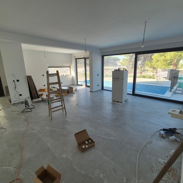 Moderná dvojposchodová vila s veľkými oknami, balkónmi a dvojgarážou s elegantným autom vpredu, ktorá sa nachádza v meste Drage v Chorvátsku.