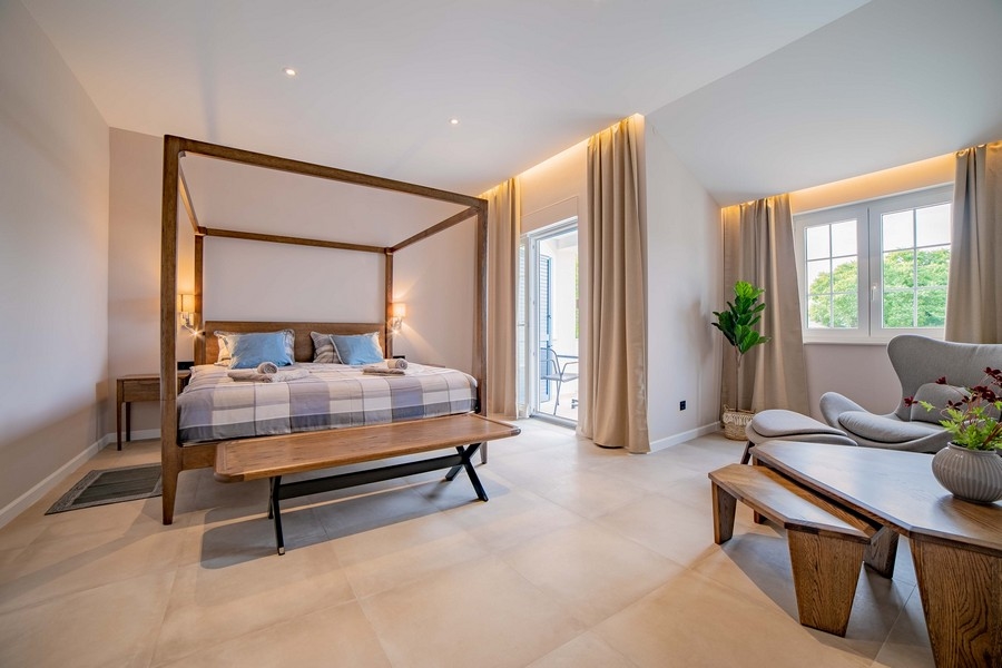 Priestranná spálňa s posteľou s baldachýnom, lavicou a pohodlným sedením, zariadená vo svetlých farbách a s množstvom prirodzeného svetla