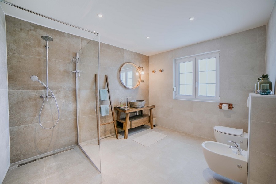 Luxusná kúpeľňa s veľkým sprchovacím kútom, bidetom a rustikálnym dreveným umývadlom v zemitých tónoch a moderným vybavením