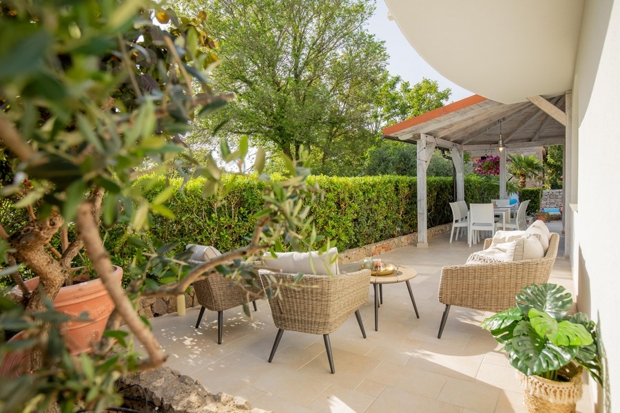 Vonkajšie posedenie s prúteným nábytkom a zatieneným jedálenským kútom obklopeným zeleňou a stromami