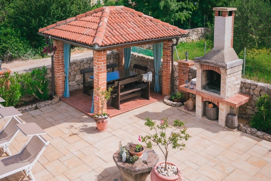 Vonkajší priestor na grilovanie s murovaným altánkom, dreveným jedálenským stolom a kamennou pecou na dláždenej terase