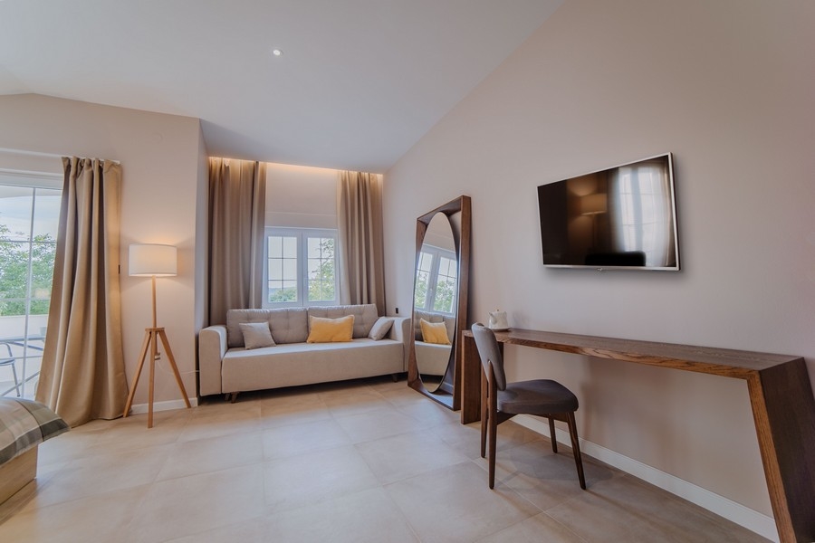 Útulná obývacia izba s niekoľkými pohovkami, TV a veľkými oknami s modrými závesmi, ktoré prepúšťajú prirodzené svetlo