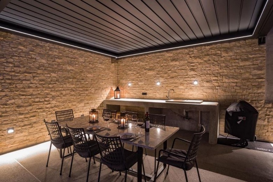 Krytý vonkajší priestor s jedálenským kútom a grilom, obklopený kamennými múrmi