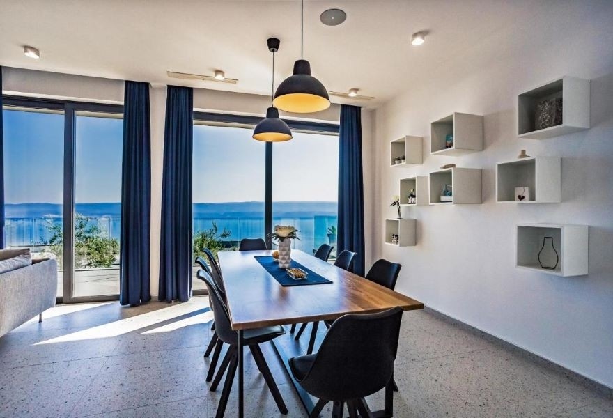 Jedáleň s moderným dreveným stolom, čiernymi stoličkami a panoramatickým výhľadom na more