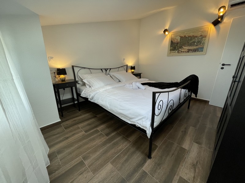 Spálňa s kovanou posteľou, drevenou podlahou a nástennými svietidlami s bočným výhľadom na obraz