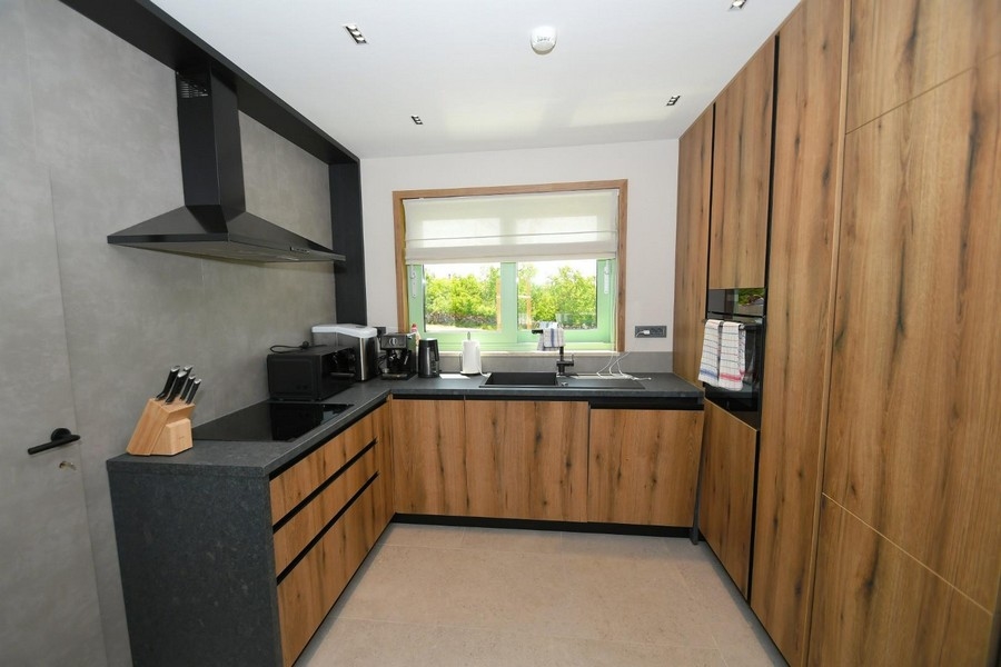 Moderná kuchyňa s dreveným obkladom, čiernymi doskami a kuchynskými spotrebičmi