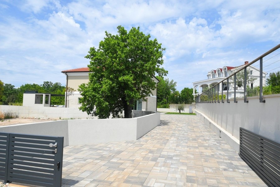 Veľká spevnená vonkajšia plocha so stromom a moderným oplotením