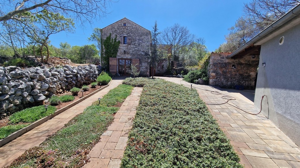 Udržiavaná záhrada so spevneným chodníkom a kamenným domom v pozadí.