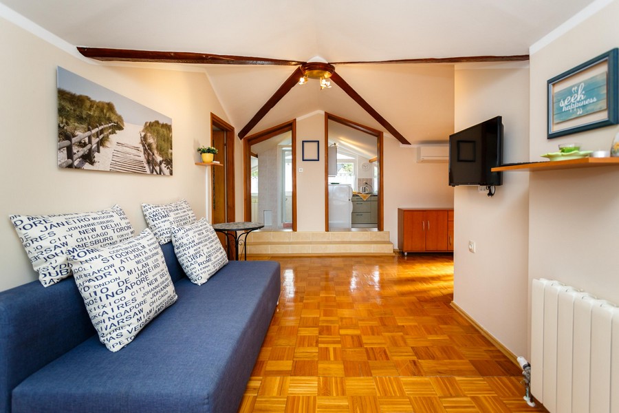 Obývacia izba s pohovkou, drevenou podlahou a trámovým stropom vedie do malej kuchyne